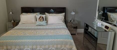 A neatly arranged bedroom with a large bed, two bedside tables, a dresser, and a mirror.