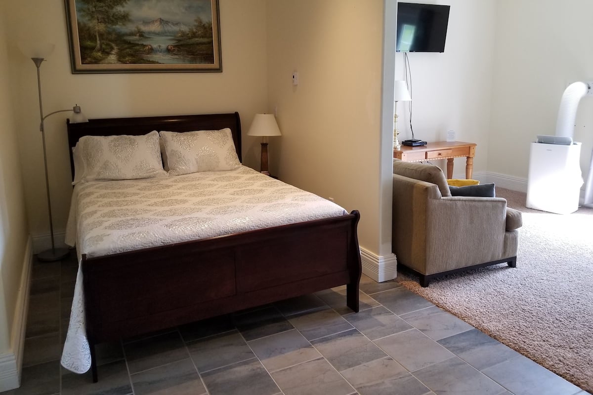 A bedroom with a bed, a desk, a chair, a TV, and a painting on the wall.