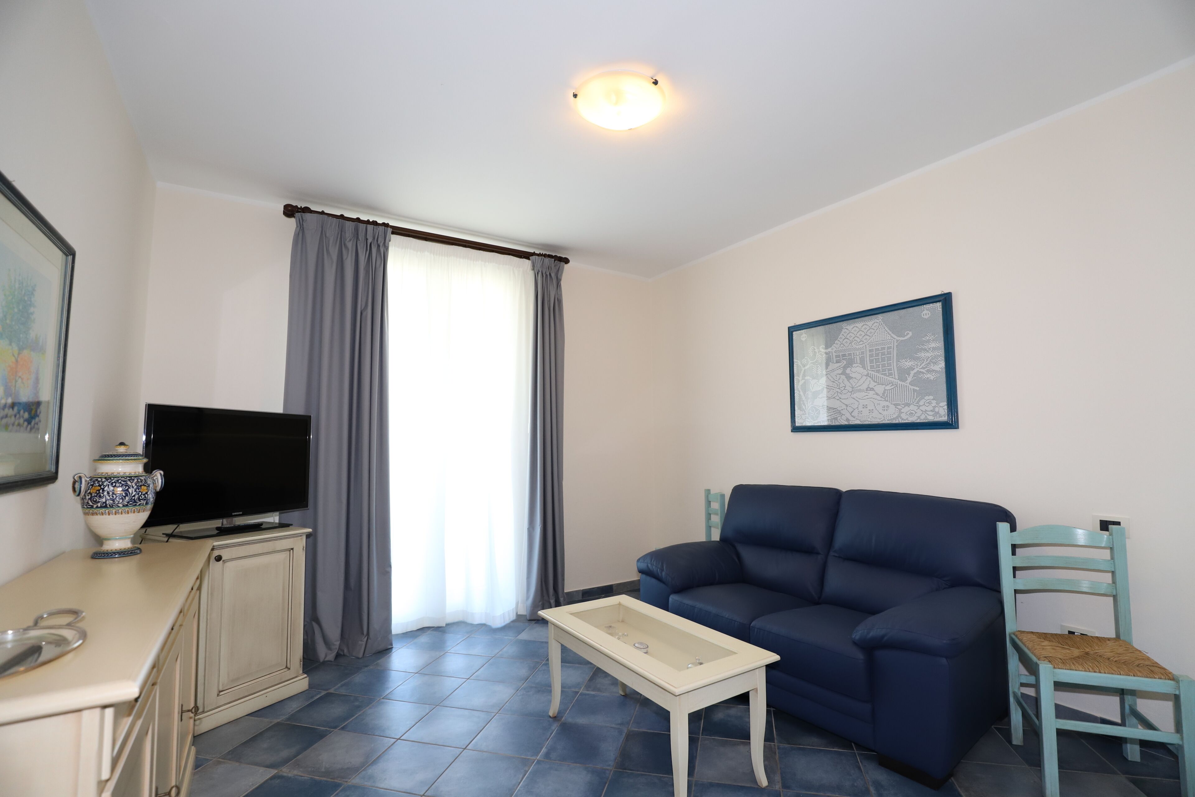 A living room with a sofa, a television, a small table, a chair, and a window with curtains.