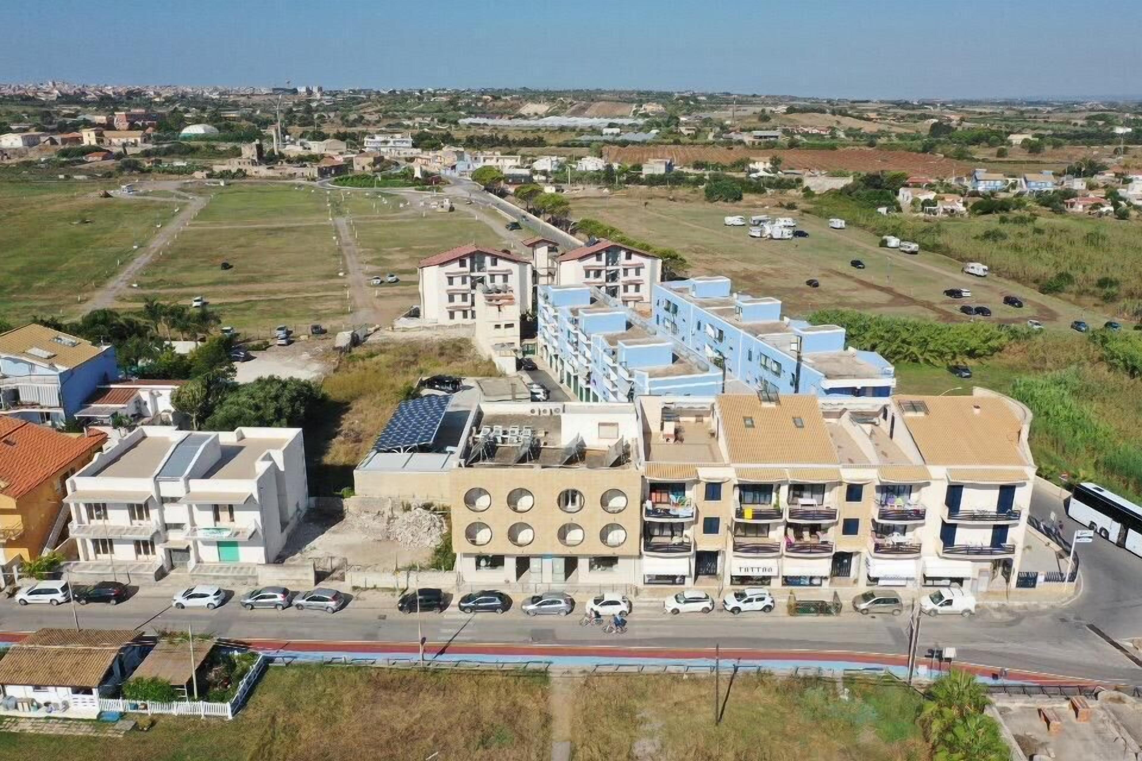 A multi-story hotel with a central courtyard, a parking lot, and a view of the surrounding landscape.