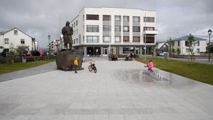 A public square with a statue, a modern building, and a wet pavement. - Gallery Guesthouse StayWest (Akranes)