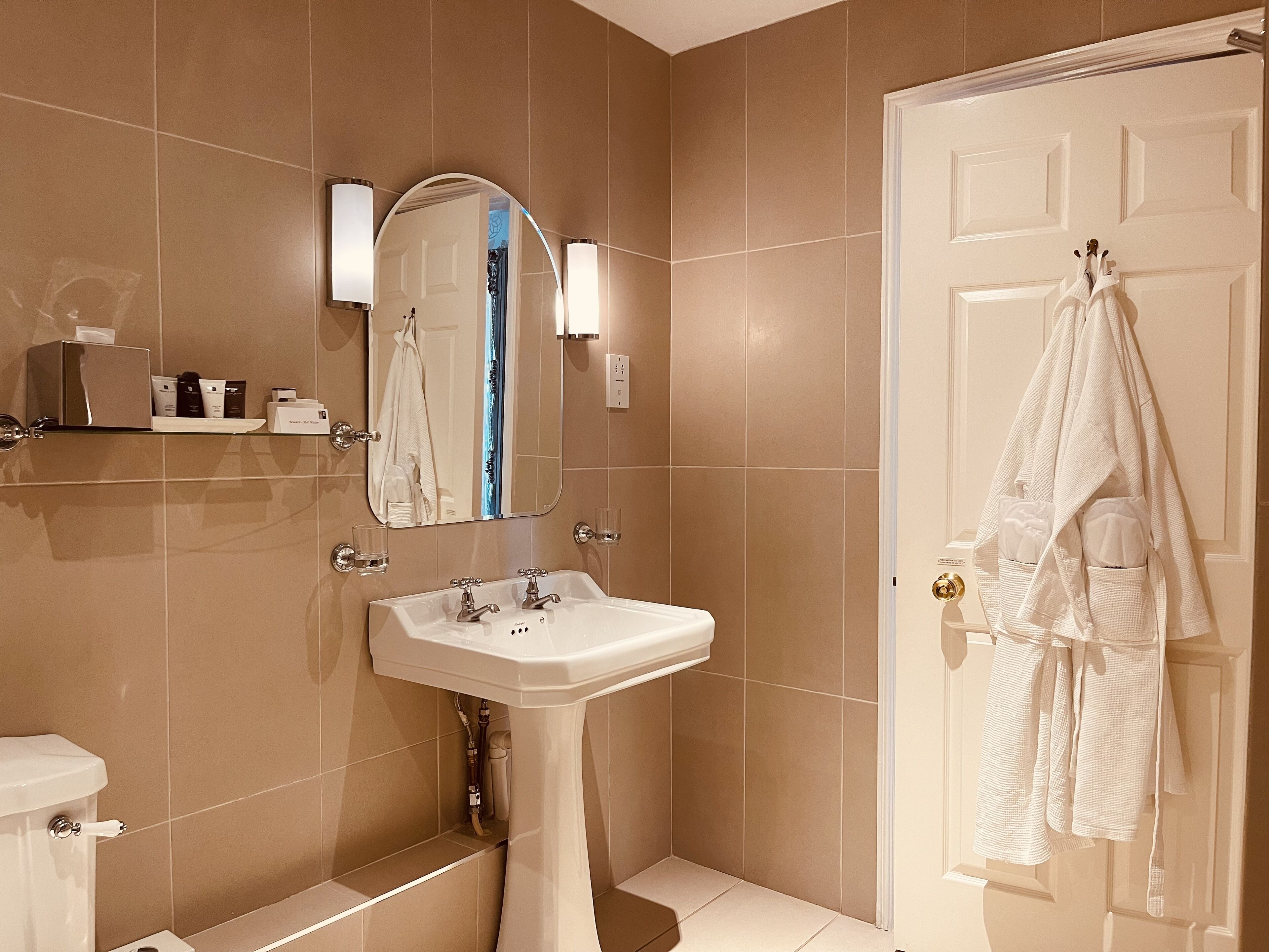 Een badkamer met een wastafel op een voetstuk, een spiegel, een handdoekhouder en een toilet.