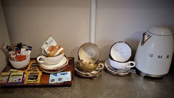 A kitchen counter with various items including a white kettle, stacked bowls, a tray with breakfast cereal packets, and a bowl of cookies.
