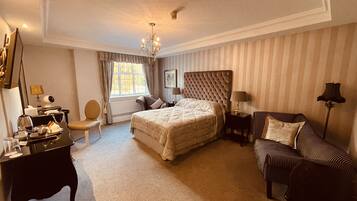 Ein Hotelzimmer mit einem großen Bett, einer Sitzecke inklusive Sofa und Sessel, einem Schreibtisch mit Telefon und Lampe sowie einem Fenster mit Vorhängen.