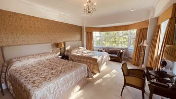 A hotel room with two beds, a desk, a chair, a chandelier, and large windows with curtains.