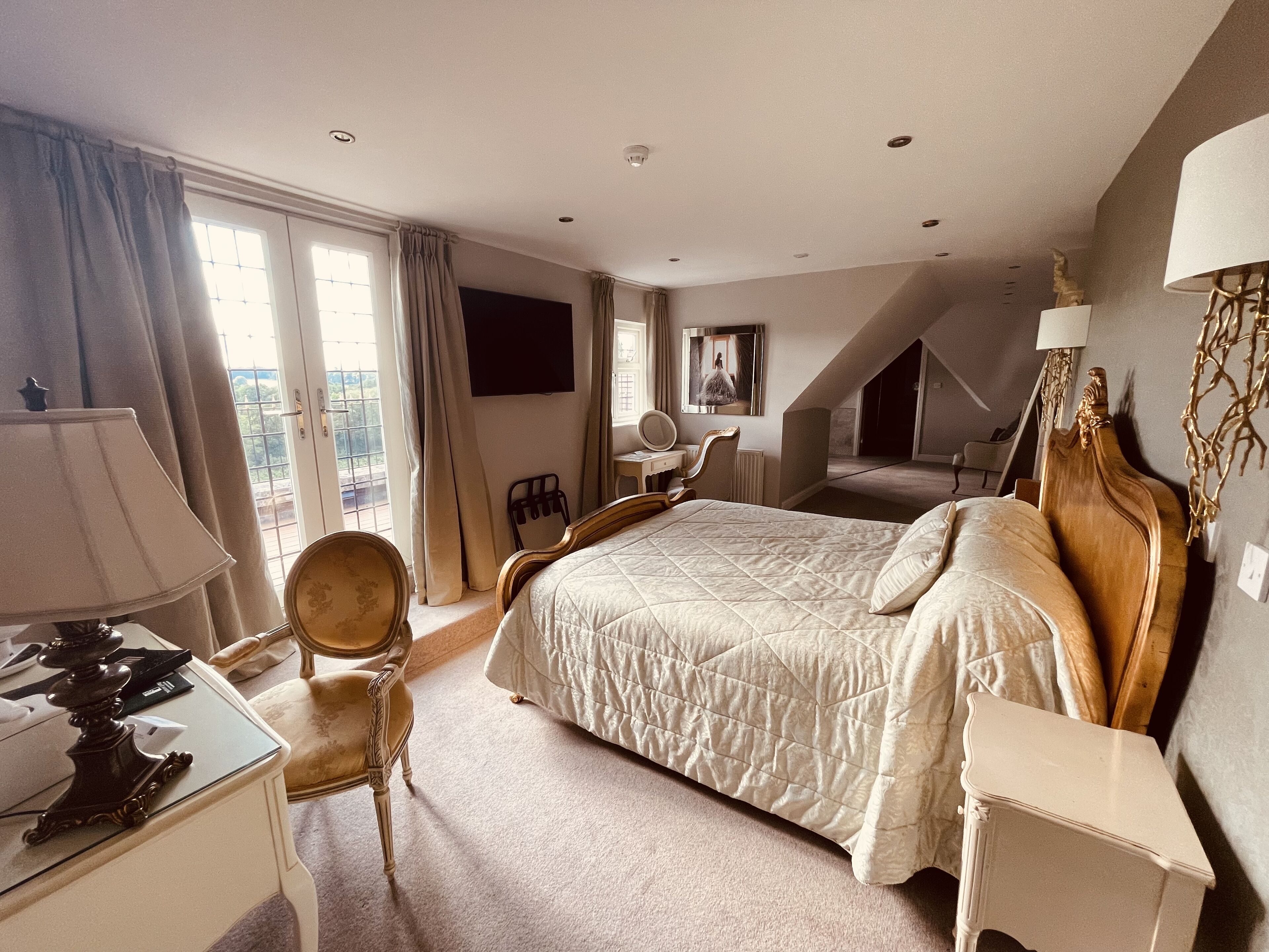 A hotel room with a large bed, a desk with a lamp, a chair, a mirror, and a view of the outdoors.