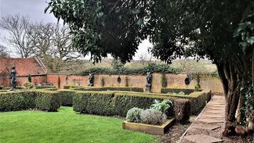 Un jardín bien cuidado con estatuas, un muro de ladrillo y un sendero.