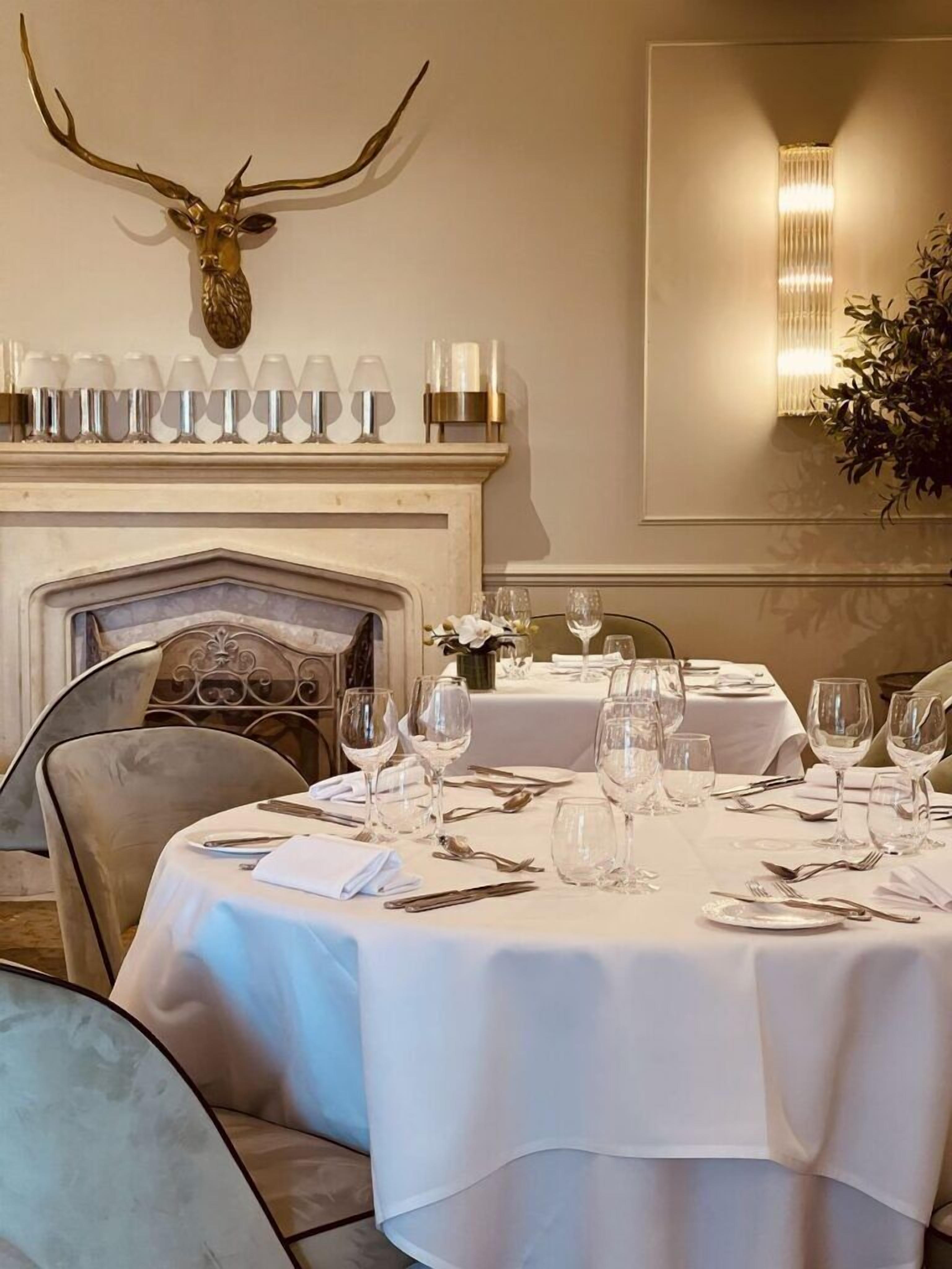 A dining room with a fireplace, a mounted deer head, and a row of wine glasses above it.