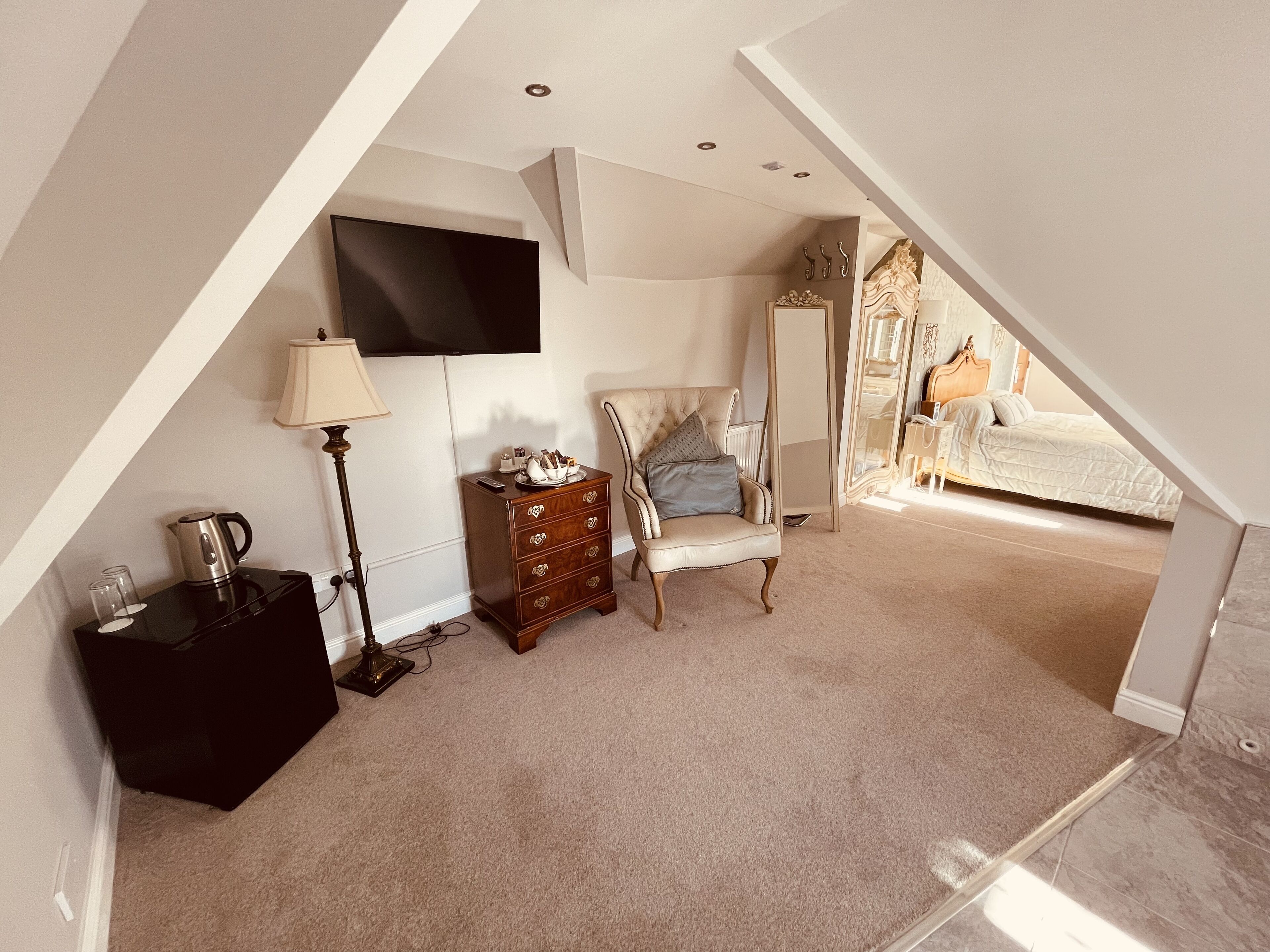 A bedroom with a TV mounted on the wall, a dresser, a chair, and a bed.