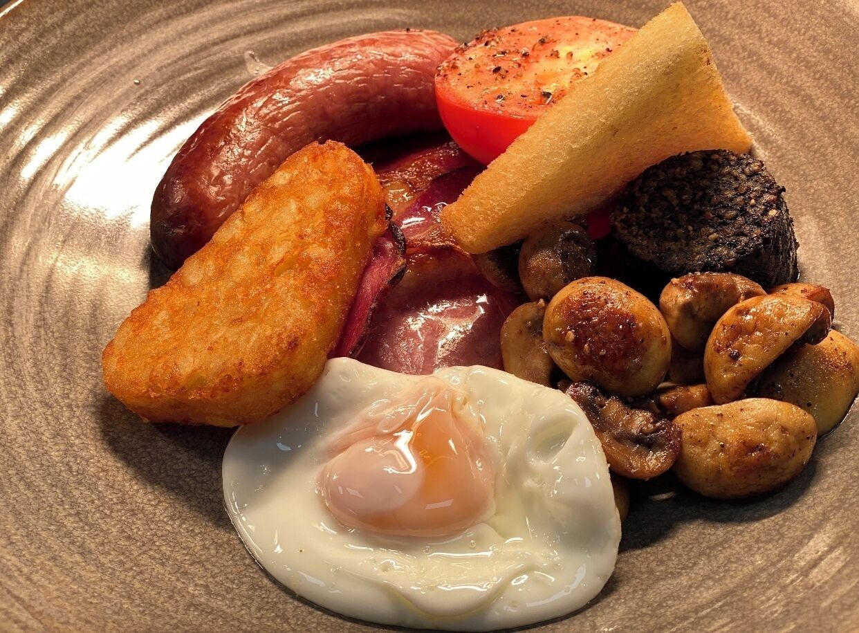 A plate of breakfast food including sausages, a fried egg, mushrooms, and toast.