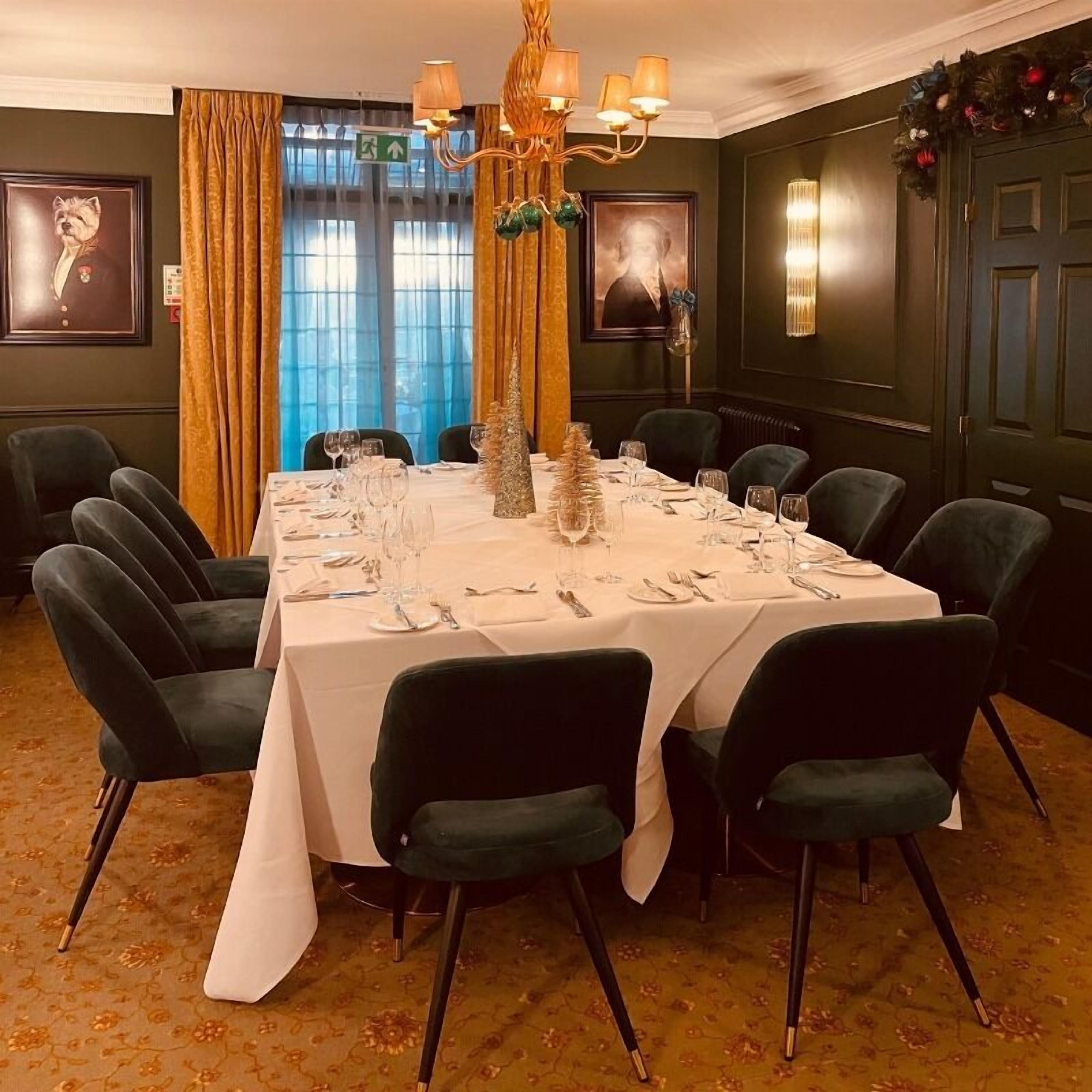 A dining room with a large table set for a meal, surrounded by dark green upholstered chairs.