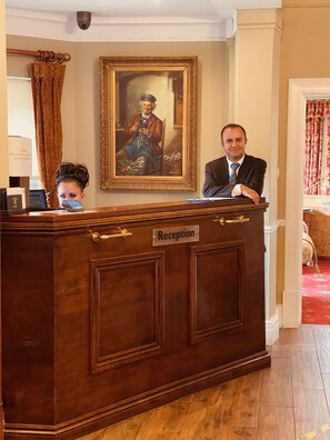 A reception desk with a sign reading "Reception," a framed portrait above it, and a person standing behind the desk.
