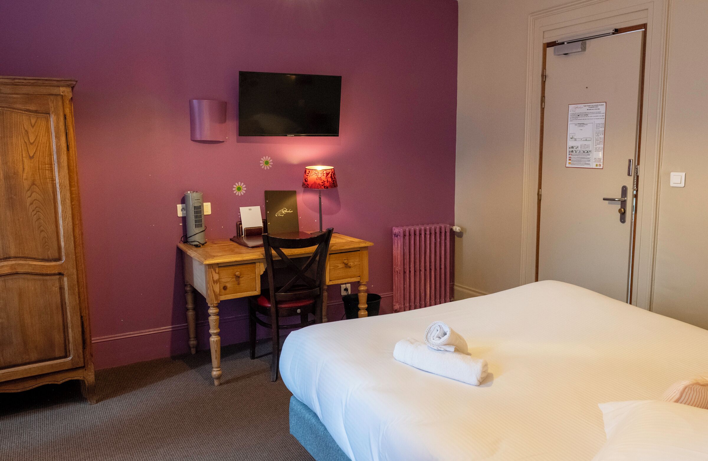 Een hotelkamer met een bed, een bureau met stoel, een televisie en een radiator.