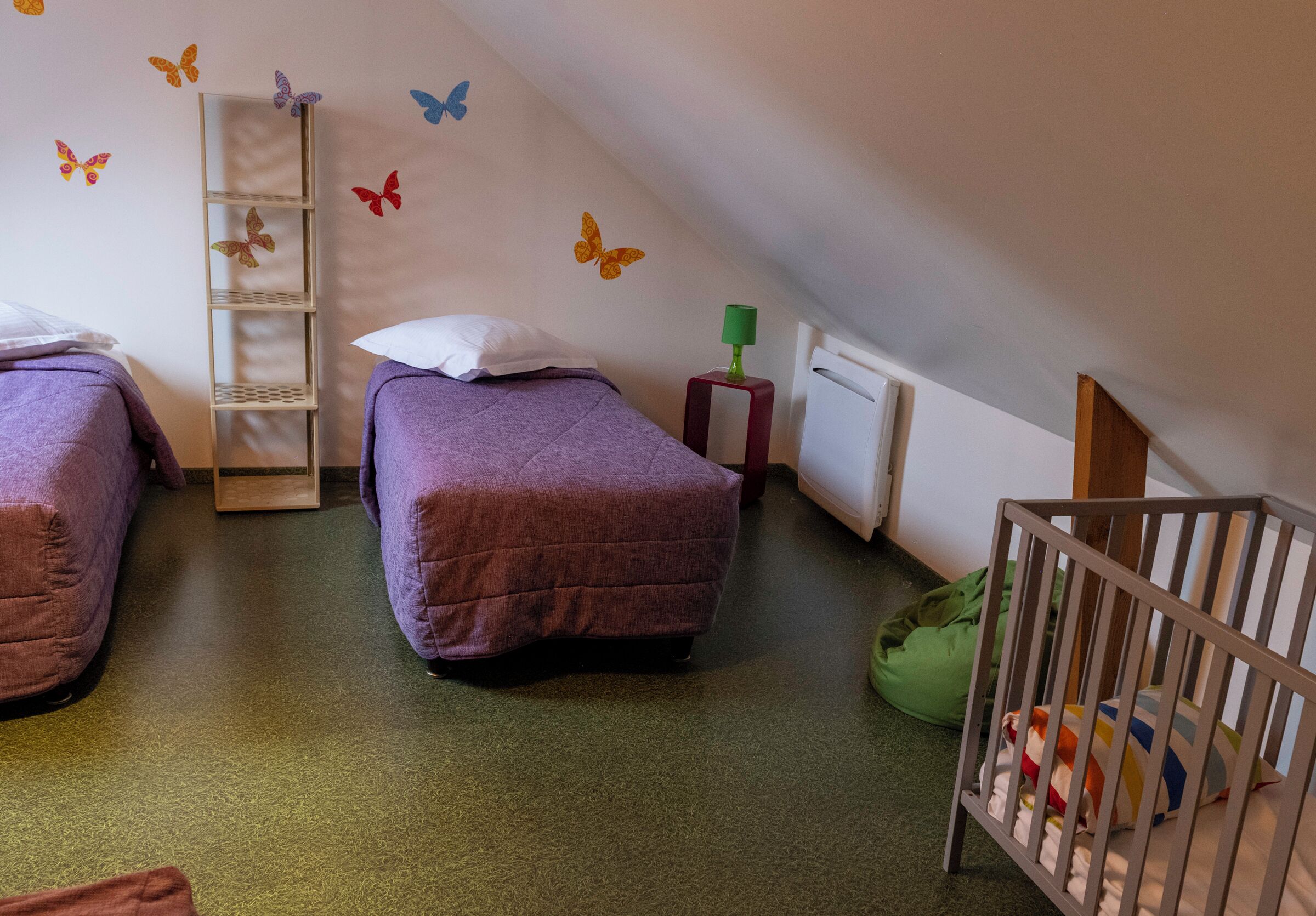 Habitación infantil con dos camas, una cuna, un radiador y decoraciones de mariposas en la pared.