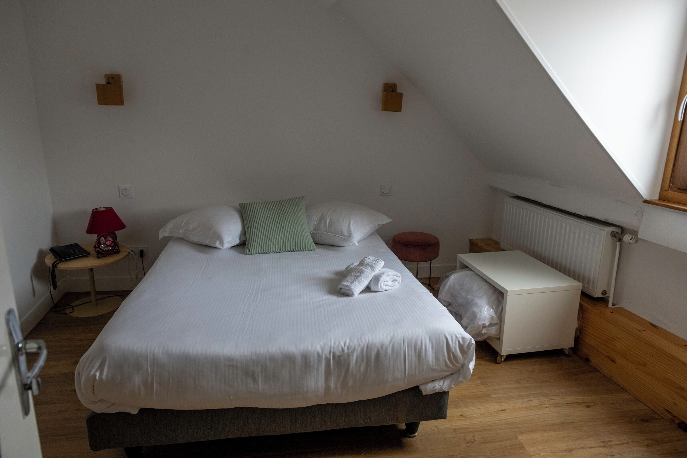Een slaapkamer met een bed, nachtkastje, lamp, radiator en raam.