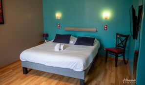 A neatly made bed with white linens and two dark pillows, a wooden nightstand with a lamp, a red chair, and a teal-colored wall with two wall-mounted lights. - Logis Hôtel La Corne d'Abondance (Grand Bourgtheroulde)
