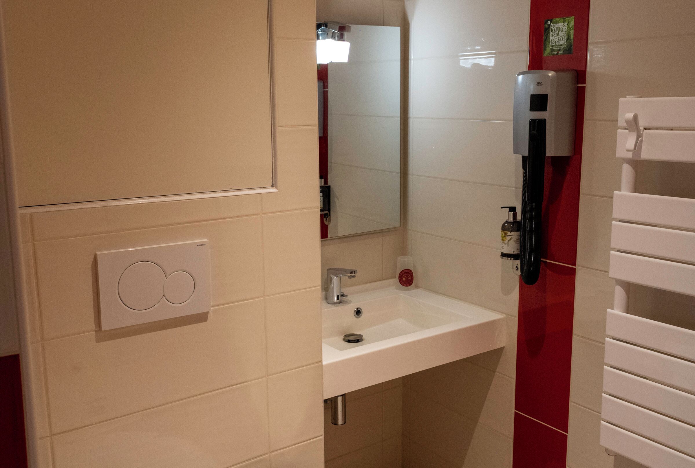 Une salle de bain avec un lavabo blanc, un miroir, un porte-serviettes et un distributeur de savon.