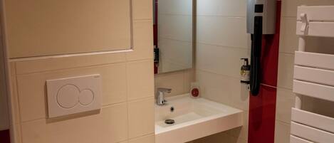 Une salle de bain avec un lavabo blanc, un miroir, un porte-serviettes et un distributeur de savon.