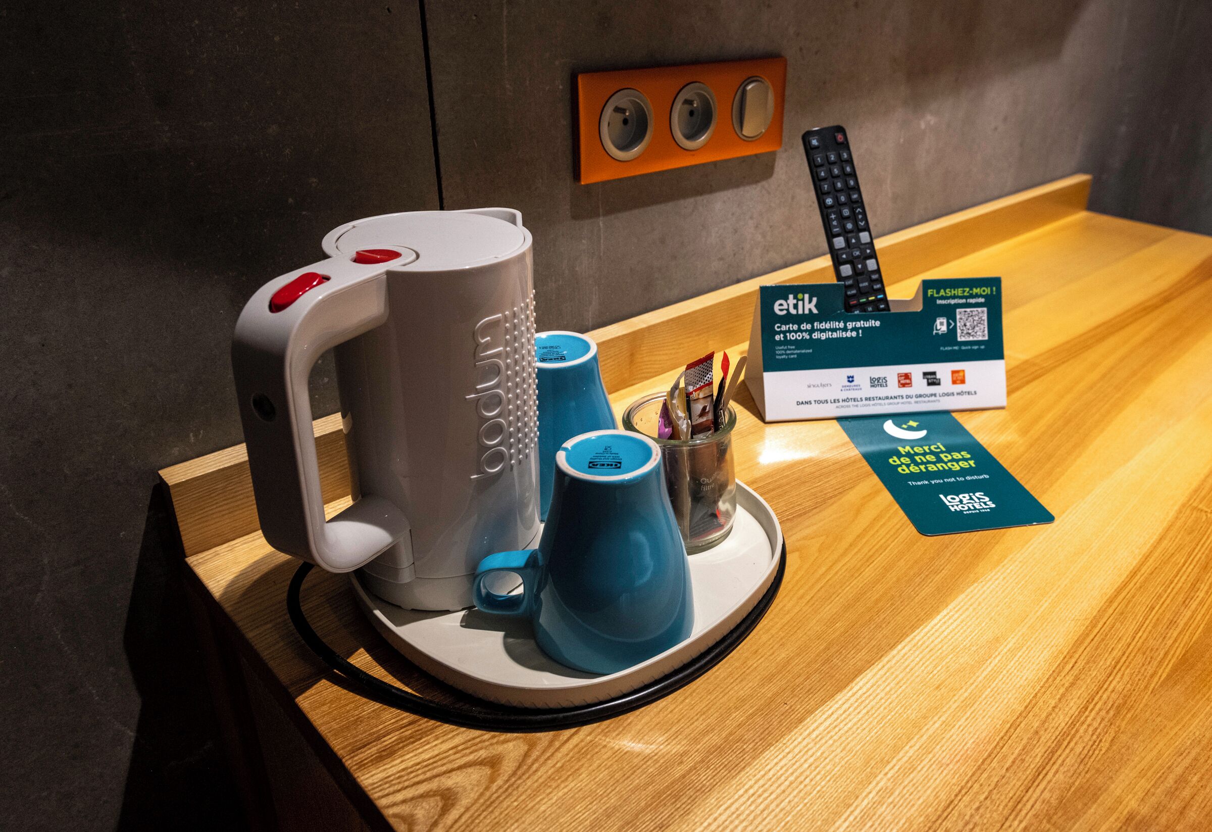 A coffee machine, a remote control, and a card reader on a wooden counter.