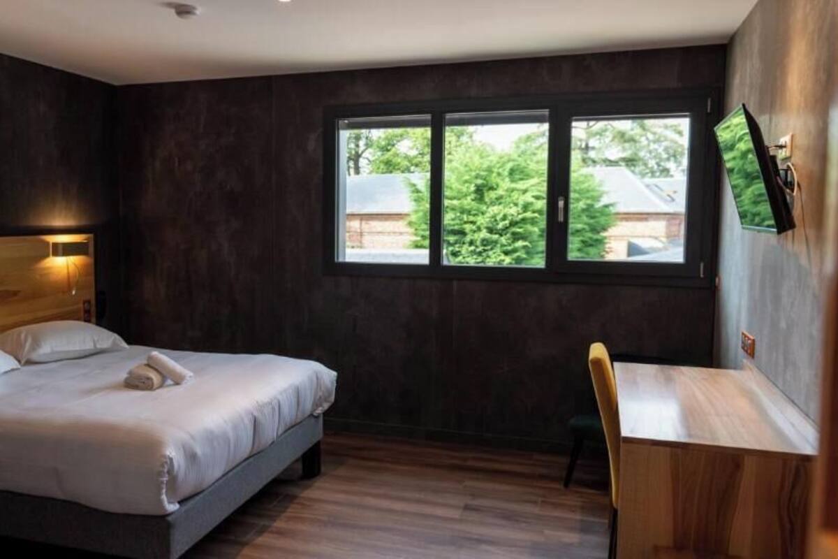 A bedroom with a bed, a desk, and a window.