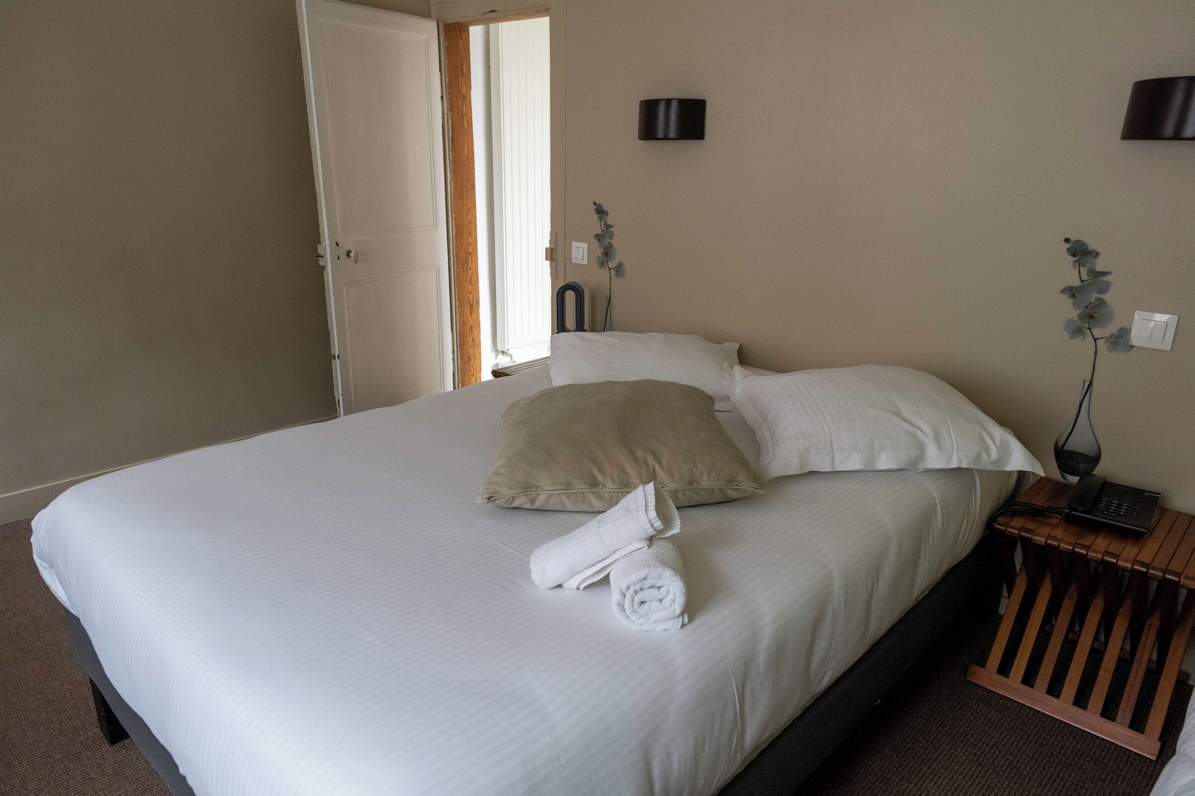 A hotel room with a large bed, a wooden nightstand, a telephone, and a wall-mounted light fixture.