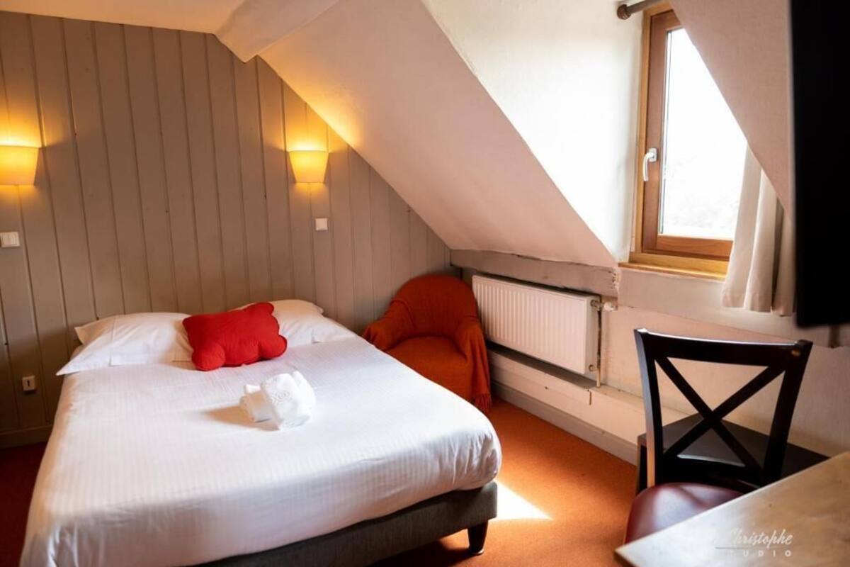 A bedroom with a bed, a red pillow, a chair, and a window.