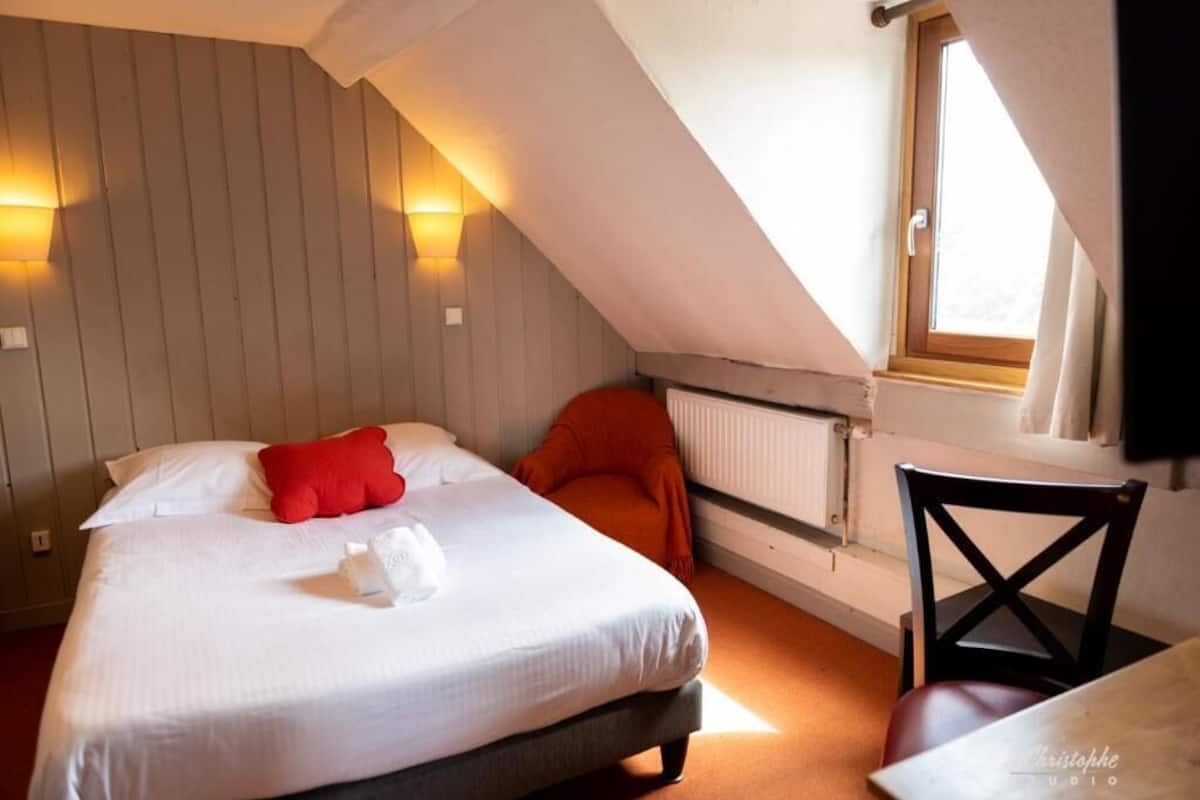 A bedroom with a bed, a red pillow, a chair, and a window.