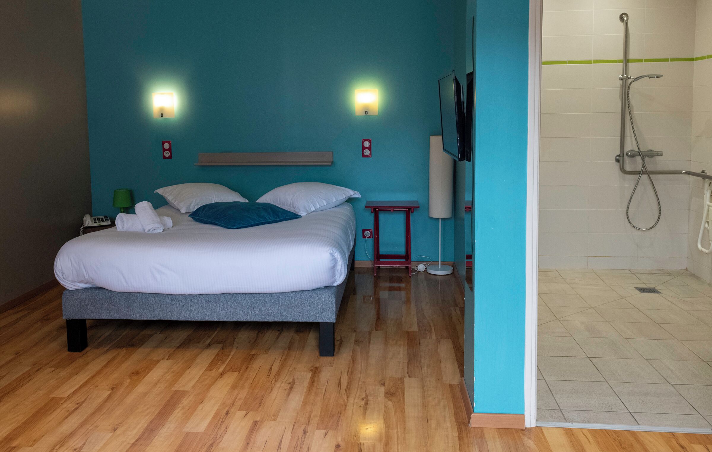 Een hotelkamer met een bed, nachtkastje, televisie, telefoon en douche.