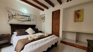 A bedroom with a bed, wooden headboard, a painting above the bed, a wooden door, and a shelf with a single item. - Hotel Casa Cantabria (Villa de Leyva)