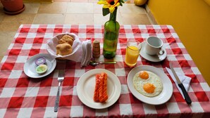 A breakfast table with a red and white checkered tablecloth, plates of eggs, toast, and juice, a vase with a flower, and a green bottle. - Hotel Casa Cantabria (Villa de Leyva)