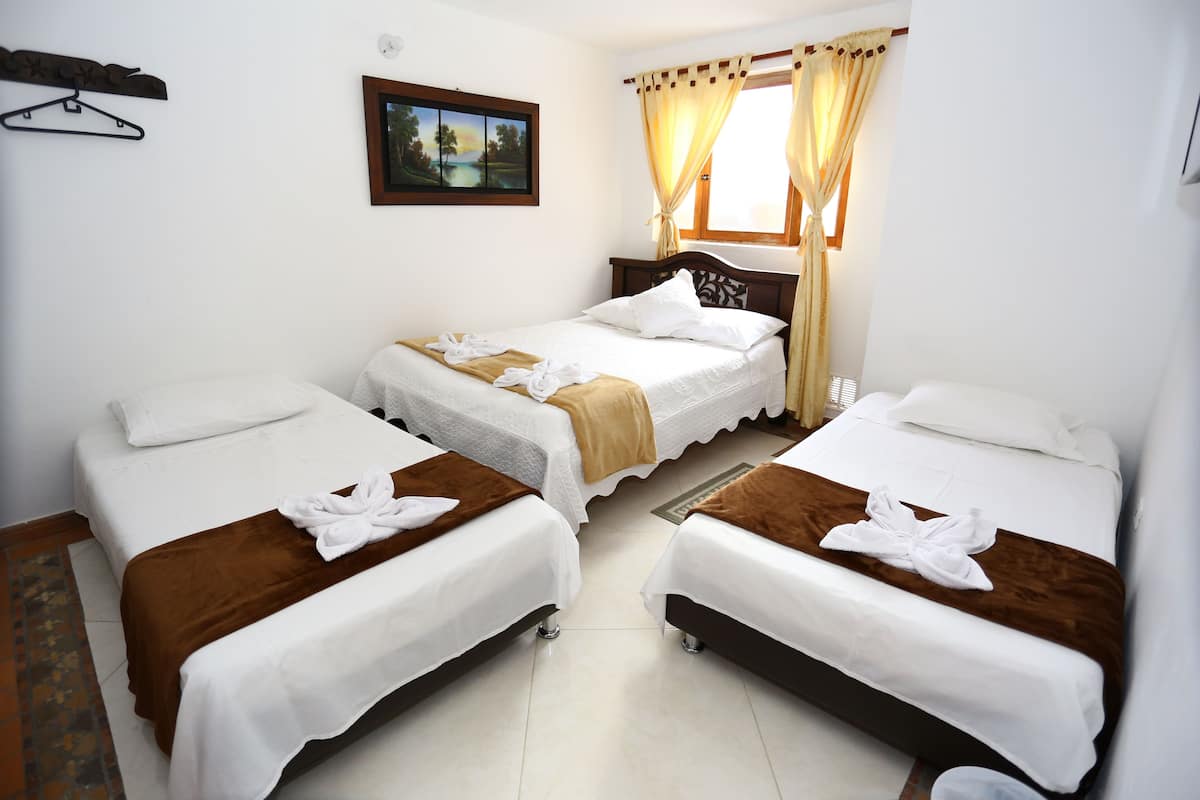 Habitación de hotel con dos camas individuales, cabecero de madera, una ventana pequeña con cortinas, un cuadro colgado en la pared y un perchero.