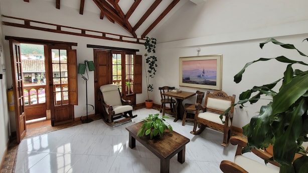 A spacious room with wooden beams, a chandelier, a dining area with wooden furniture, and a large window with a view of greenery. - Hotel Casa Cantabria (Villa de Leyva)