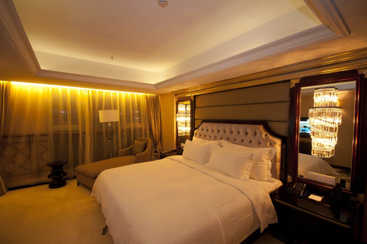 Una habitación de hotel con una cama grande, una zona de estar, un candelabro y un espejo.