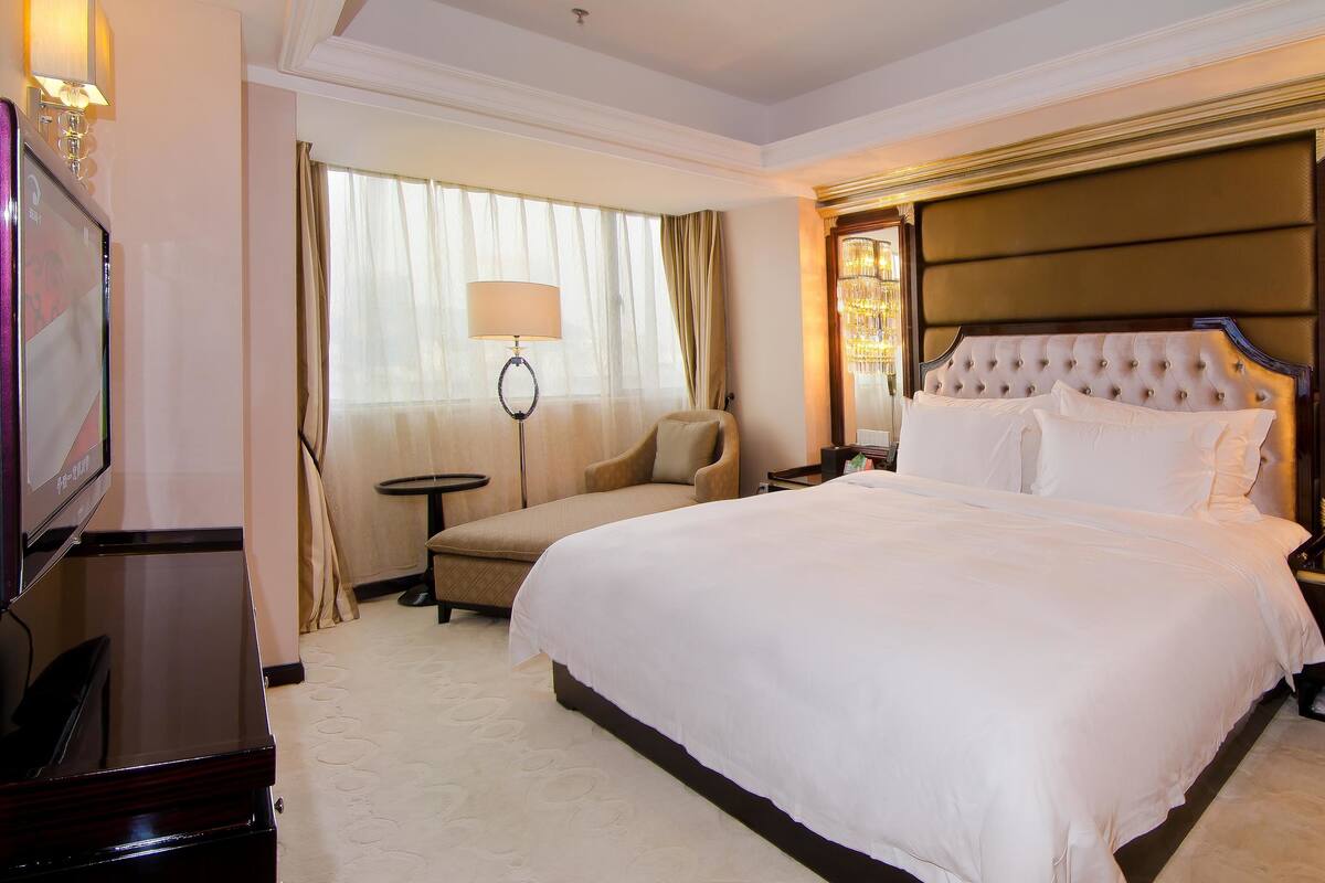 Habitación de hotel con una cama grande, televisión, escritorio, silla y candelabro.