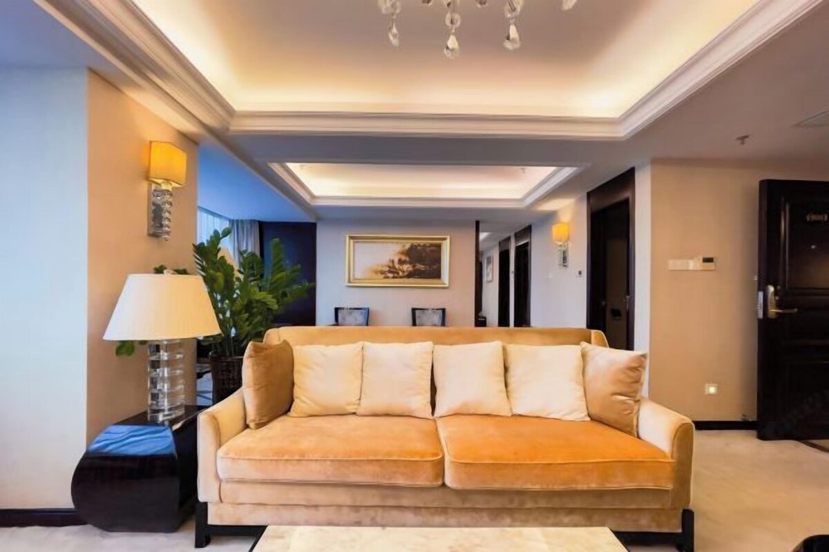 A modern living room with a beige sofa, a side table with a lamp, and a potted plant.