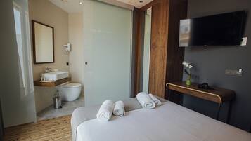 A modern hotel room with a large bed, a wooden desk, a flat-screen TV, a bathroom with a toilet and sink, and a mirror.