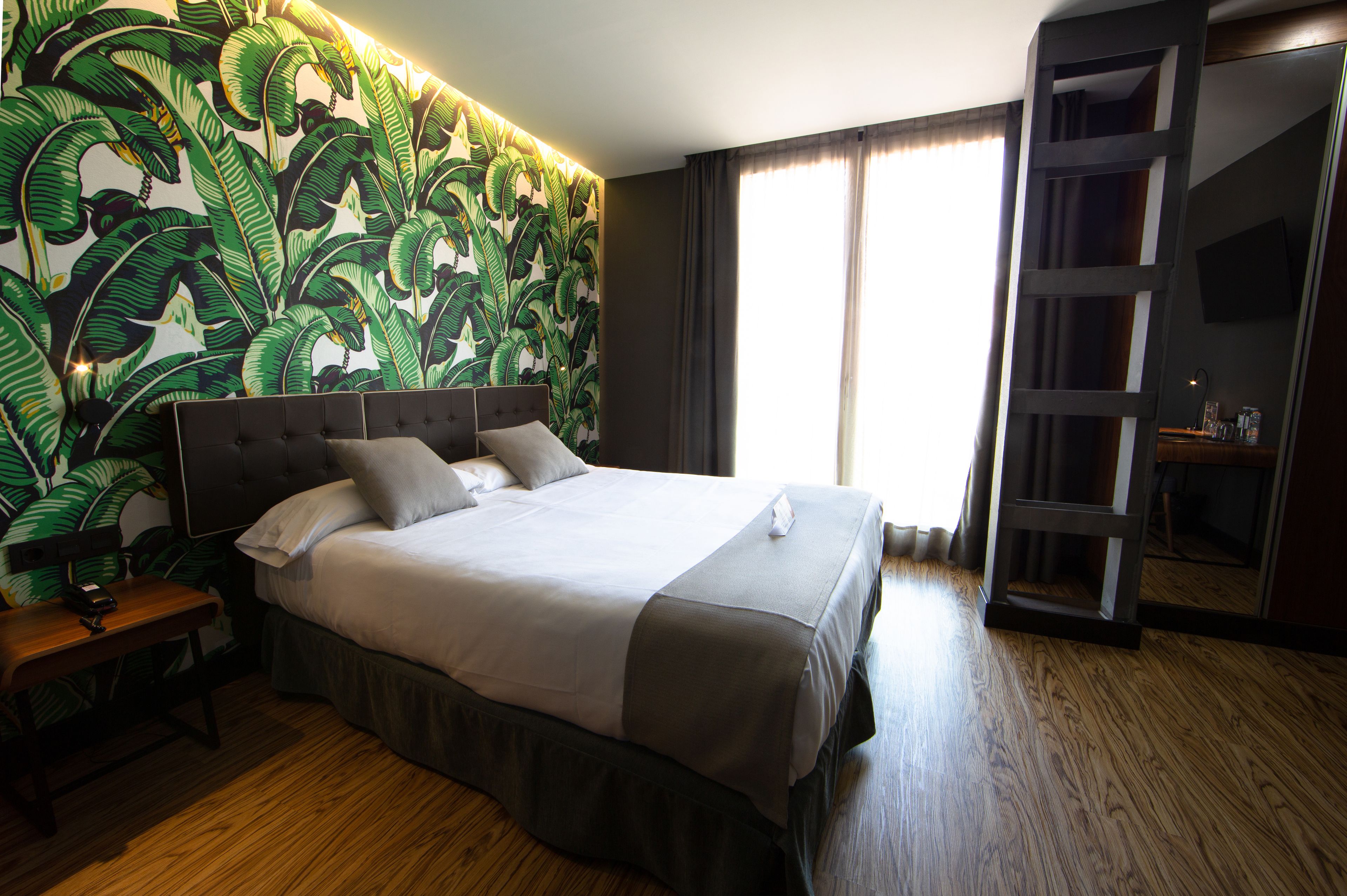 Habitación de hotel con una cama grande, una mesita de noche, un escritorio, un armario y un espejo amplio.