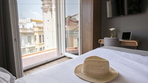 A hotel room with a large window, a bed with a straw hat, a desk with a laptop, and a TV on the wall. - Málaga Premium Hotel (Málaga)