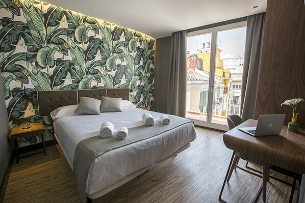 A hotel room with a large bed, a laptop on a wooden table, and a view of the city through the window. - Málaga Premium Hotel (Málaga)
