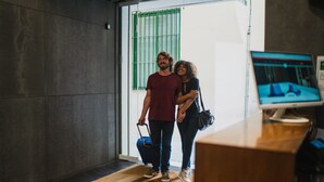 A man and a woman standing in a lobby with a wooden reception desk and a computer monitor displaying a bed image. - Málaga Premium Hotel (Málaga)