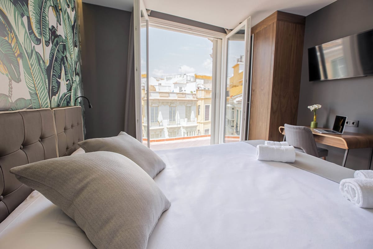 Habitación de hotel con una cama grande, televisión montada en la pared y balcón con vista a la ciudad.