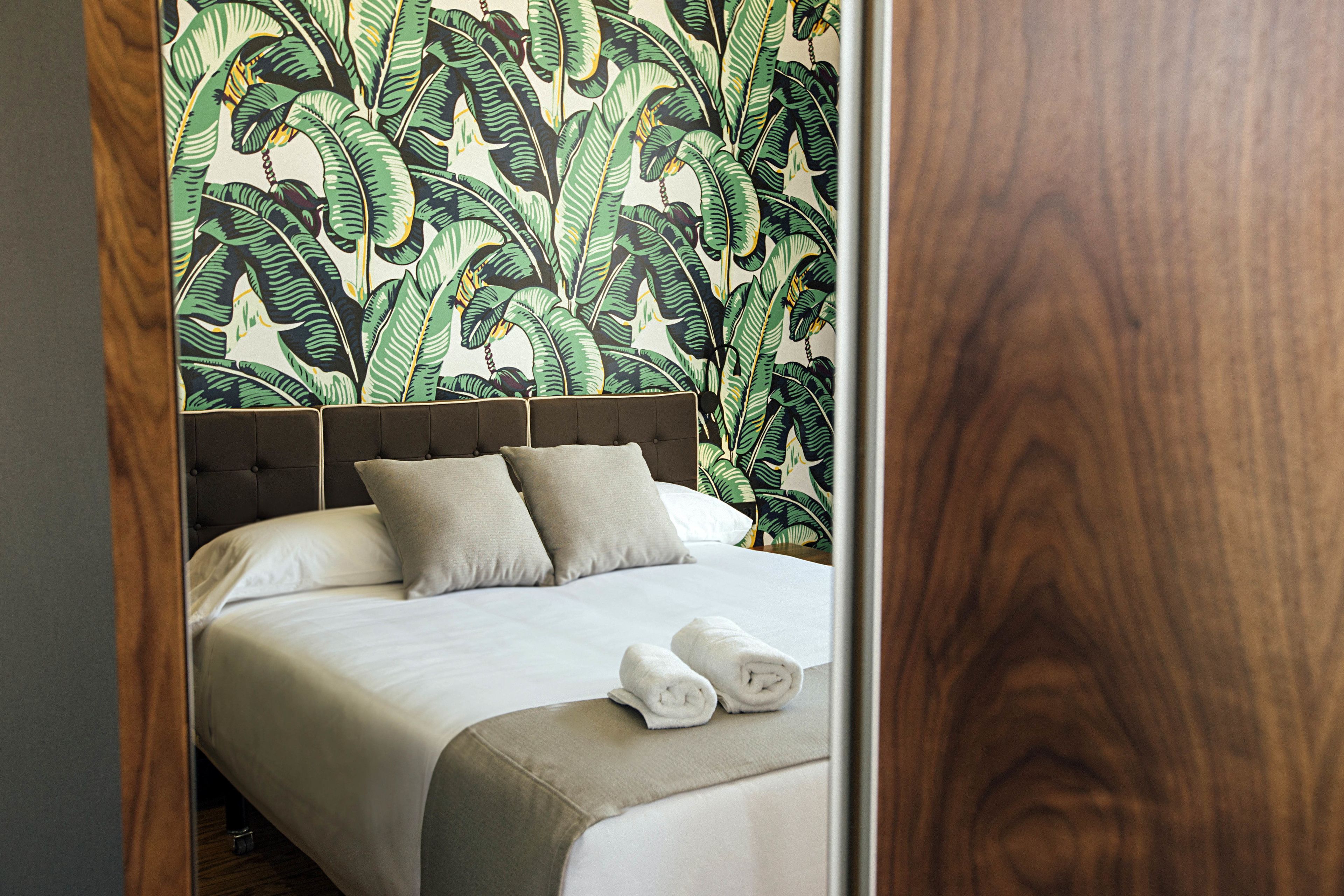 Cama bem arrumada com cabeceira, duas almofadas e dois rolinhos de toalha.