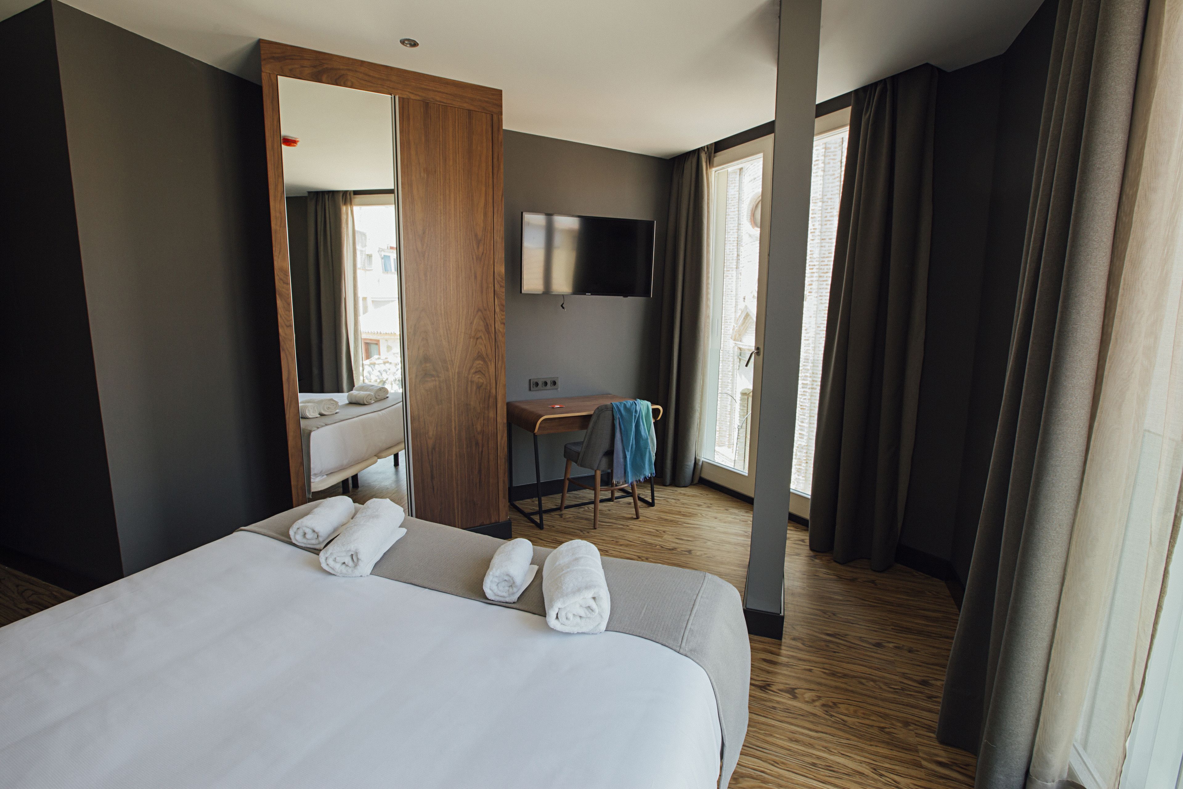 Une chambre d’hôtel avec un grand lit, un bureau, une chaise, une télévision et une fenêtre avec des rideaux.