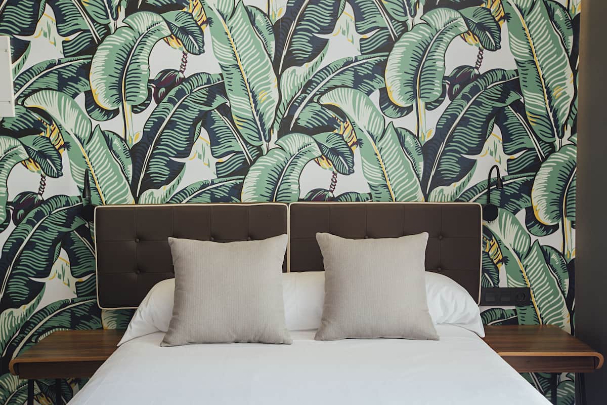 Una cama con cabecera, dos almohadas y una mesita de noche de madera.