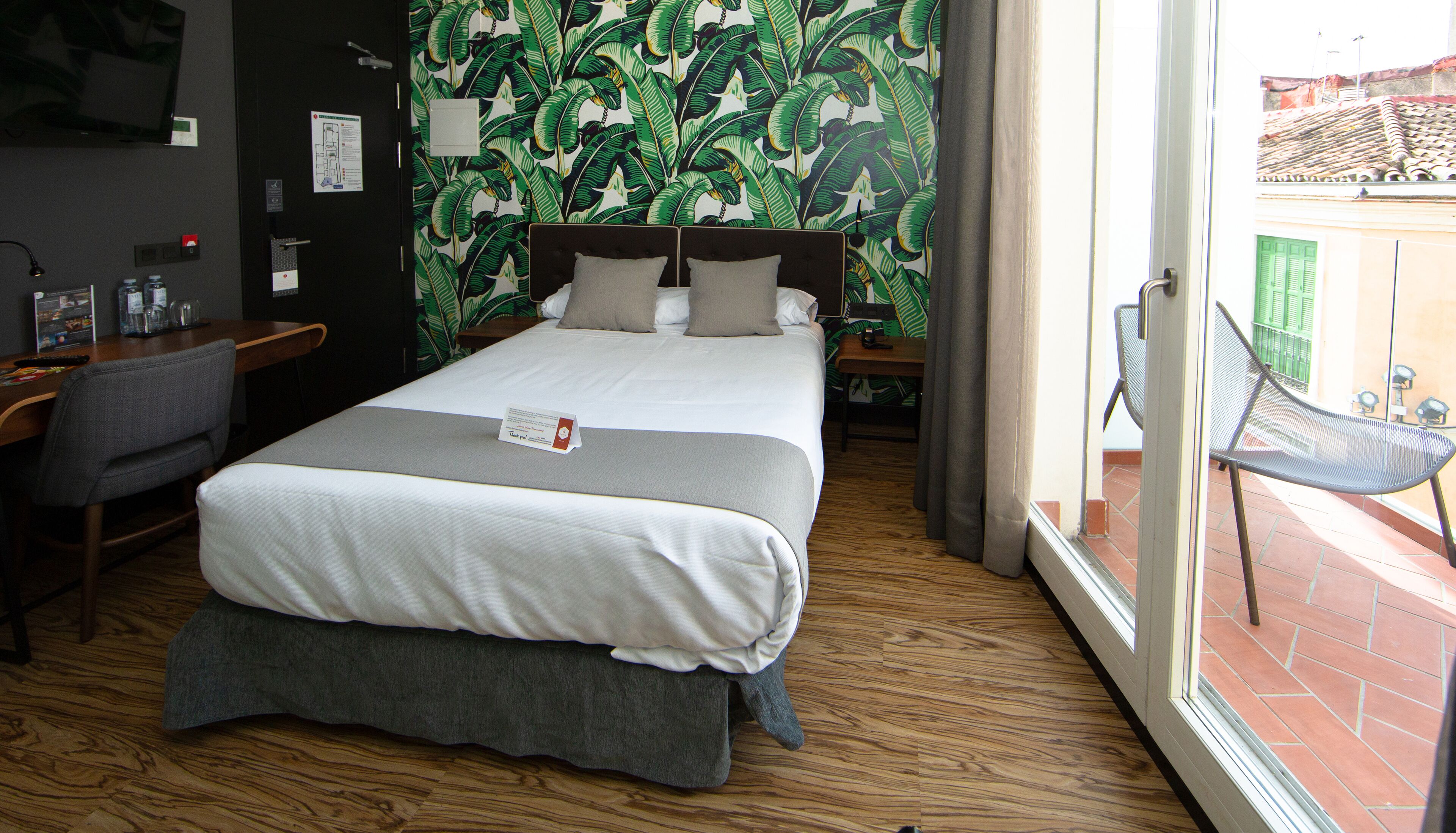 A hotel room with a large bed, a desk, a chair, and a view of the outside.