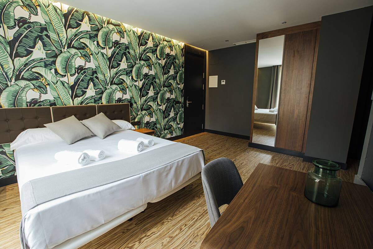 Una habitación de hotel con una cama grande, piso de madera, un espejo y una pequeña mesa.