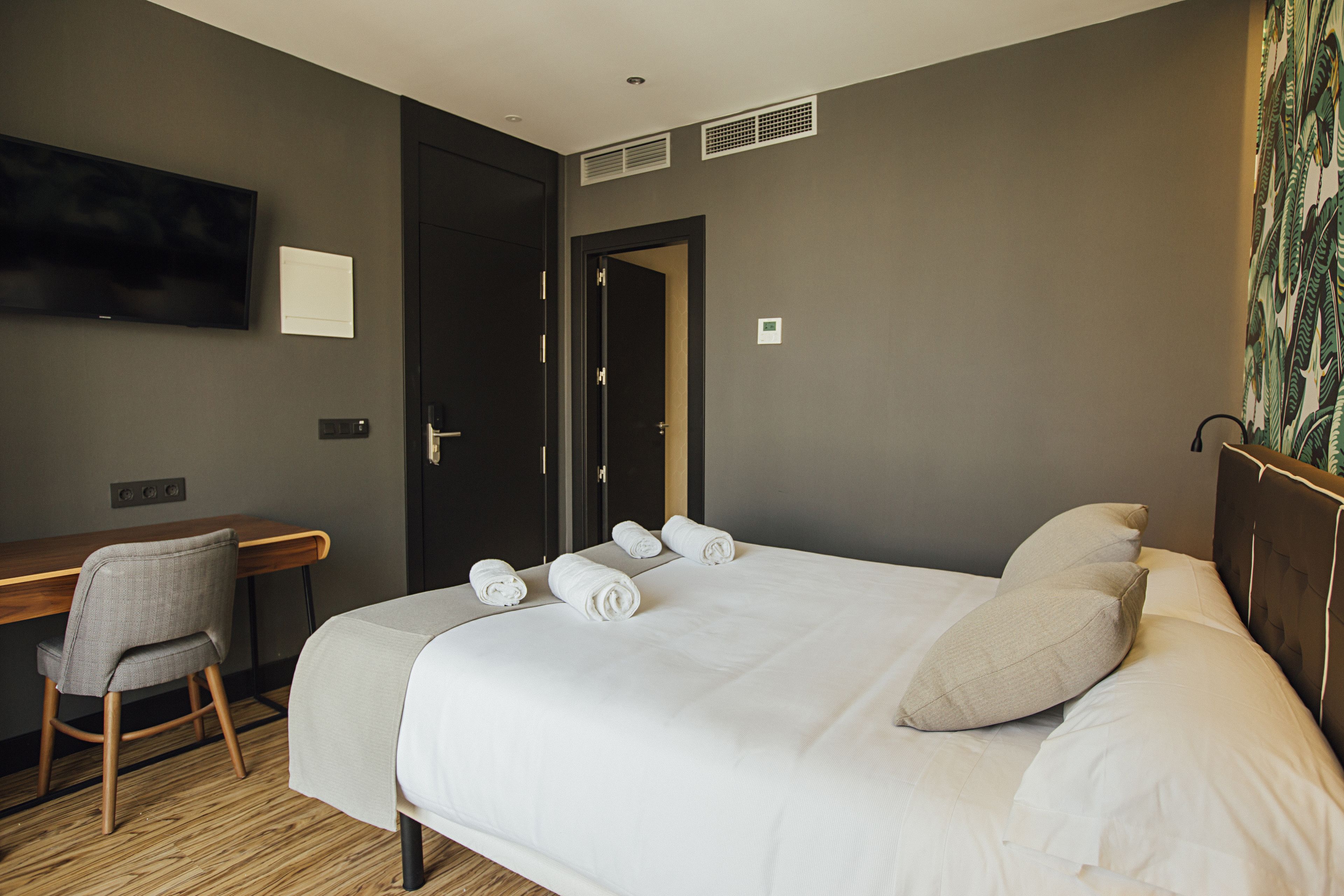 A hotel room with a bed, a desk, a chair, a television, and a door.