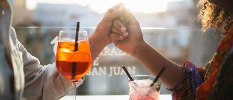 Two people holding hands at a table with drinks, overlooking a cityscape.