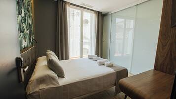 A hotel room with a bed, a wooden chair, a window with curtains, and a door with a handle.