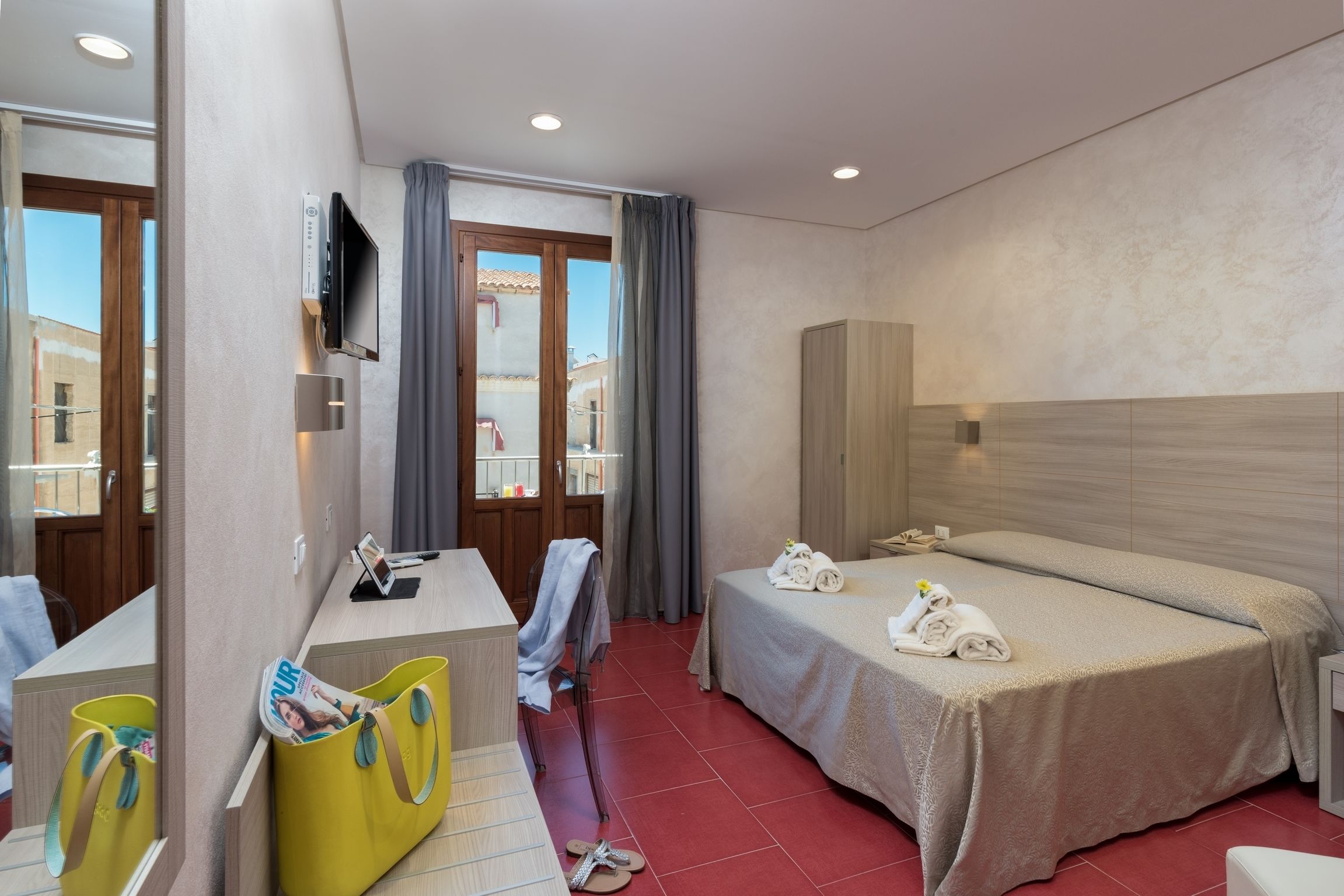 A hotel room with a bed, a desk with a TV, a bathroom, and a view of the outside.